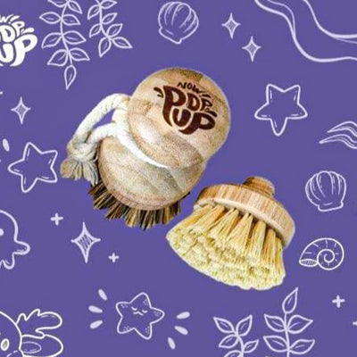 This eco-friendly pot scrubber is crafted from renewable bamboo and plant-based fibers, elegantly engraved with the 'NOW POP UP' brand insignia. Includes one complimentary replacement head, presented against a luxurious violet backdrop.