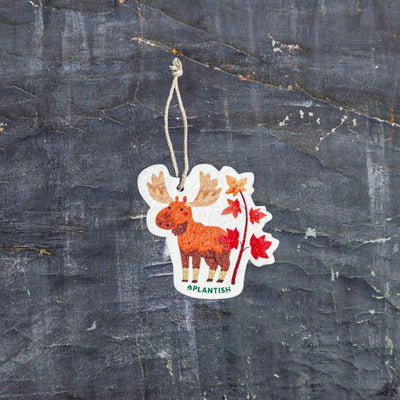 Top view of an Autumn Moose eco-friendly cellulose pop-up kitchen sponge with hanging cord, featuring a charming red moose beside a maple tree design - lying flat when dry and expanding when wet for seasonal cleaning with natural charm.