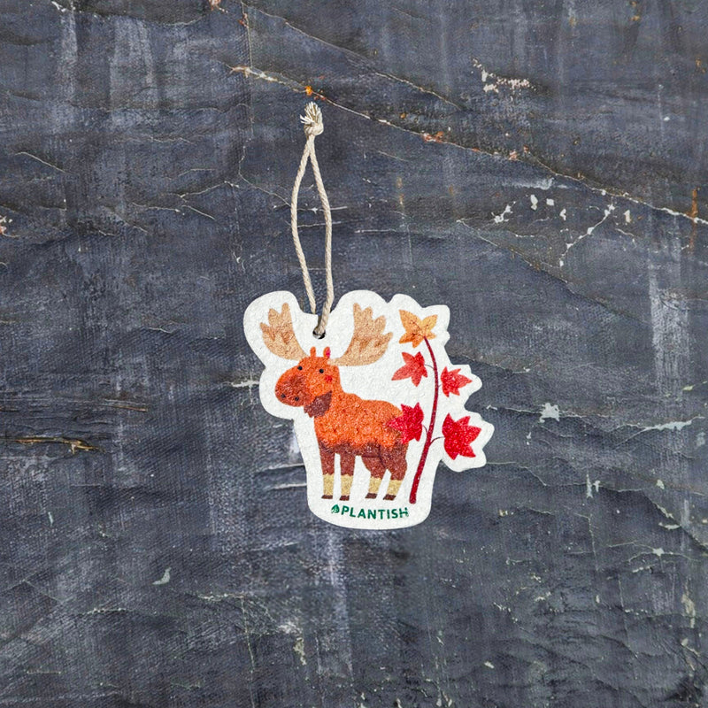 Top view of an Autumn Moose eco-friendly cellulose pop-up kitchen sponge with hanging cord, featuring a charming red moose beside a maple tree design - lying flat when dry and expanding when wet for seasonal cleaning with natural charm.