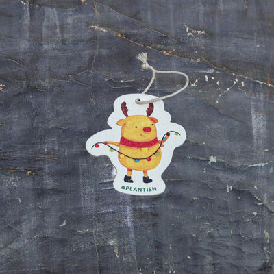 Top view of an eco-friendly cellulose pop-up kitchen sponge with hanging cord, featuring a festive holiday moose wearing a red scarf and holding string lights - compact when dry and expanding when wet for cheerful cleaning.