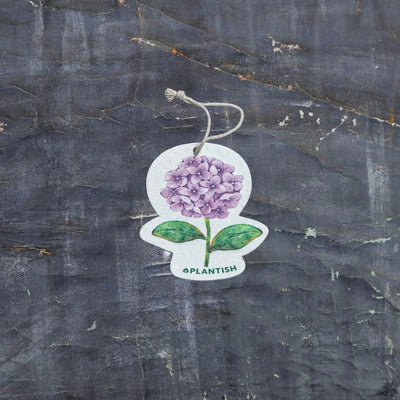 Top view of an eco-friendly cellulose pop-up kitchen sponge with hanging cord, featuring a lovely purple hydrangea design. This sustainable cleaning tool lies completely flat when dry for compact storage, then expands significantly when wet for optimal absorbency. Crafted from biodegradable plant-based cellulose, the sponge showcases a beautiful floral pattern that adds elegance to your kitchen while being gentle on the environment. 