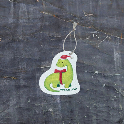 Top view of an eco-friendly cellulose pop-up kitchen sponge with hanging cord, featuring an adorable holiday dinosaur wearing a red Santa hat and red bow tie - lying flat when dry and expanding when wet for festive yet functional cleaning.