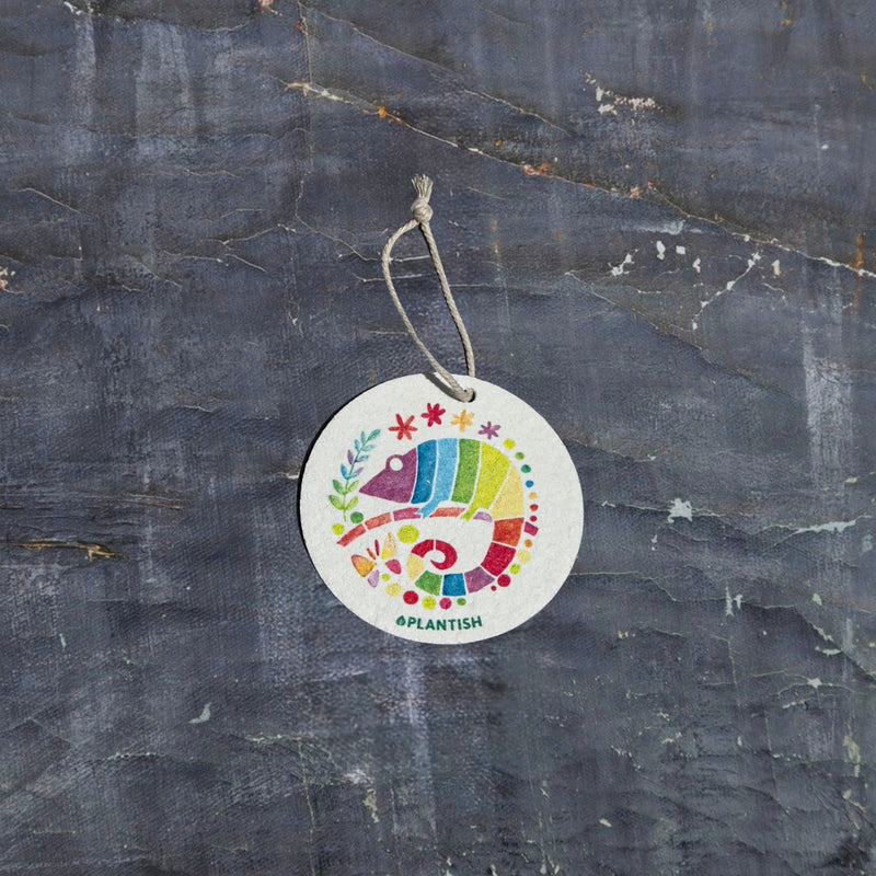 This top-view showcases an environmentally-friendly pop-up kitchen sponge crafted from biodegradable cellulose. Adorned with a colorful chameleon pattern, the practical cleaning tool features an attached hanging cord and transforms from flat/dry to expanded/wet, merging sustainable functionality with eye-catching design.