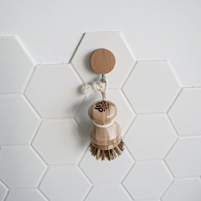 Wooden dish brush with a wooden handle on a white tiled wall