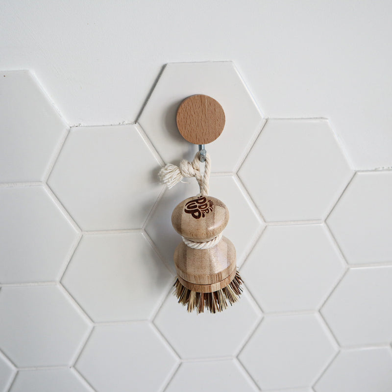 Wooden dish brush with a wooden handle on a white tiled wall