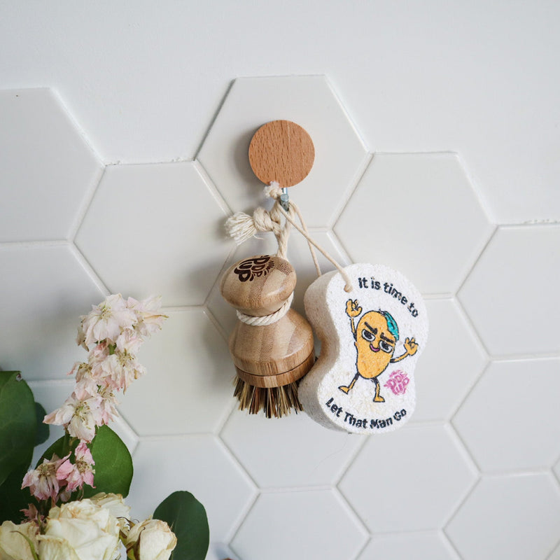 Hand holding the wooden scrubbing brush over a soap bar with a sponge and bottle in the background on a marble surface