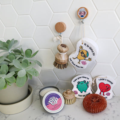 This eco-friendly cleaning set includes a wooden pot scrubber for gentle scouring, three charming white sponges featuring playful mango, frog, and heart designs, a durable red Copper Scrubby for tough stains, and a zero-waste Dish Soap Cake for sustainable dishwashing—combining functionality, style, and environmental care.