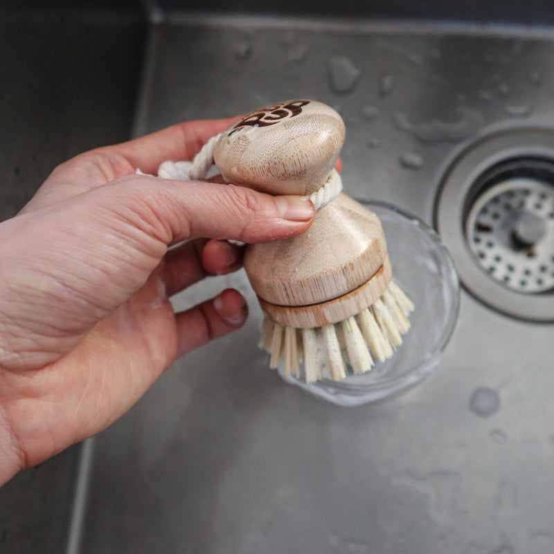 Hand holding the wooden pot scrubber with a sink in the background