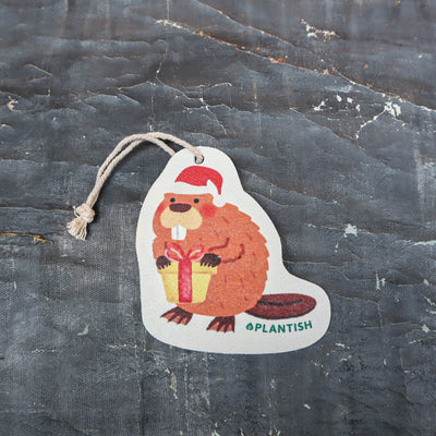 Top view of an eco-friendly cellulose pop-up kitchen sponge with hanging cord, featuring an adorable holiday beaver design wearing a red Santa hat and holding a red gift. This sustainable cleaning tool transforms from completely flat when dry to fully expanded when wet, combining festive cheer with practical functionality. Made from biodegradable plant-based cellulose, the seasonal sponge adds holiday spirit to your kitchen routine while being environmentally responsible.