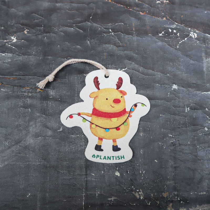Top view of an eco-friendly cellulose pop-up kitchen sponge with hanging cord, featuring a festive holiday moose wearing a red scarf and holding string lights - compact when dry and expanding when wet for cheerful cleaning.
