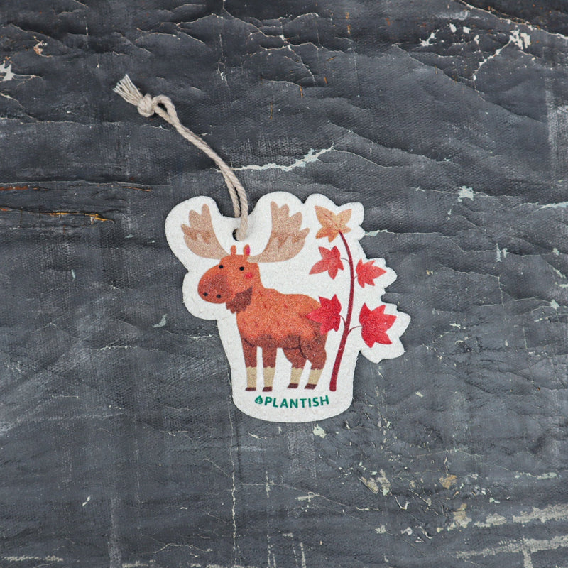 Top view of an Autumn Moose eco-friendly cellulose pop-up kitchen sponge with hanging cord, featuring a charming red moose beside a maple tree design - lying flat when dry and expanding when wet for seasonal cleaning with natural charm.