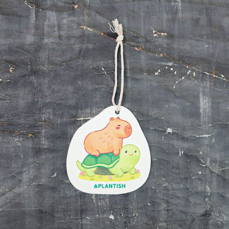 Top view of eco-friendly cellulose pop-up sponge for kitchen use. Flat, compact disc shape with a thin string attached. Design features a cute capybara riding on a turtle&