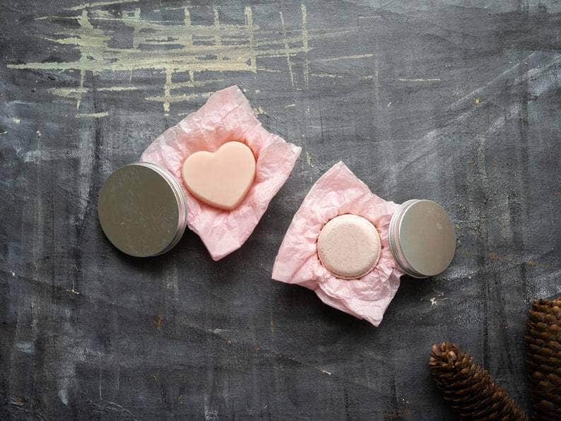 Top wide shot: Plantish Future Beauty and Bathroom Pink Nourishing Circular-shaped Shampoo and Heart-shaped Conditioner Bar Set laying on pink tissue paper in round metal tins. 