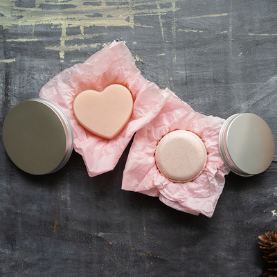 Top view: Plantish Future Beauty and Bathroom Pink Nourishing Circular-shaped Shampoo and Heart-shaped Conditioner Bar Set laying in pink tissue paper on round metal tins.